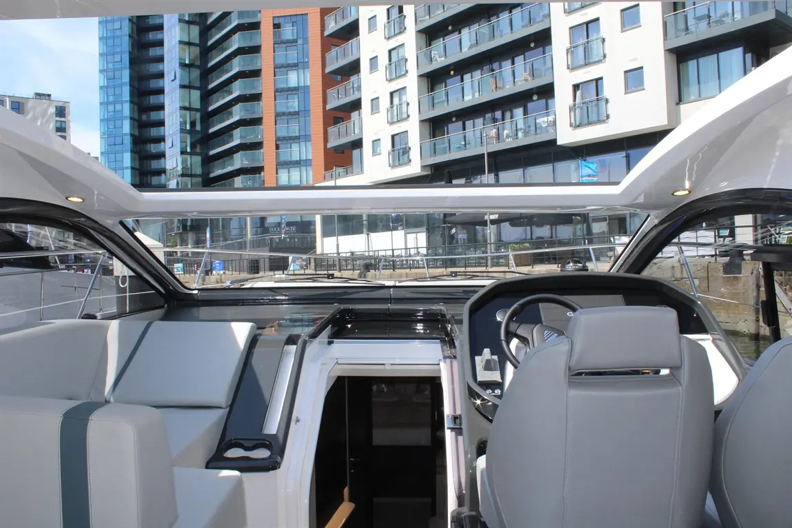 Interior view of a modern boat, featuring a steering wheel, seating area, and luxury flats in the background.
